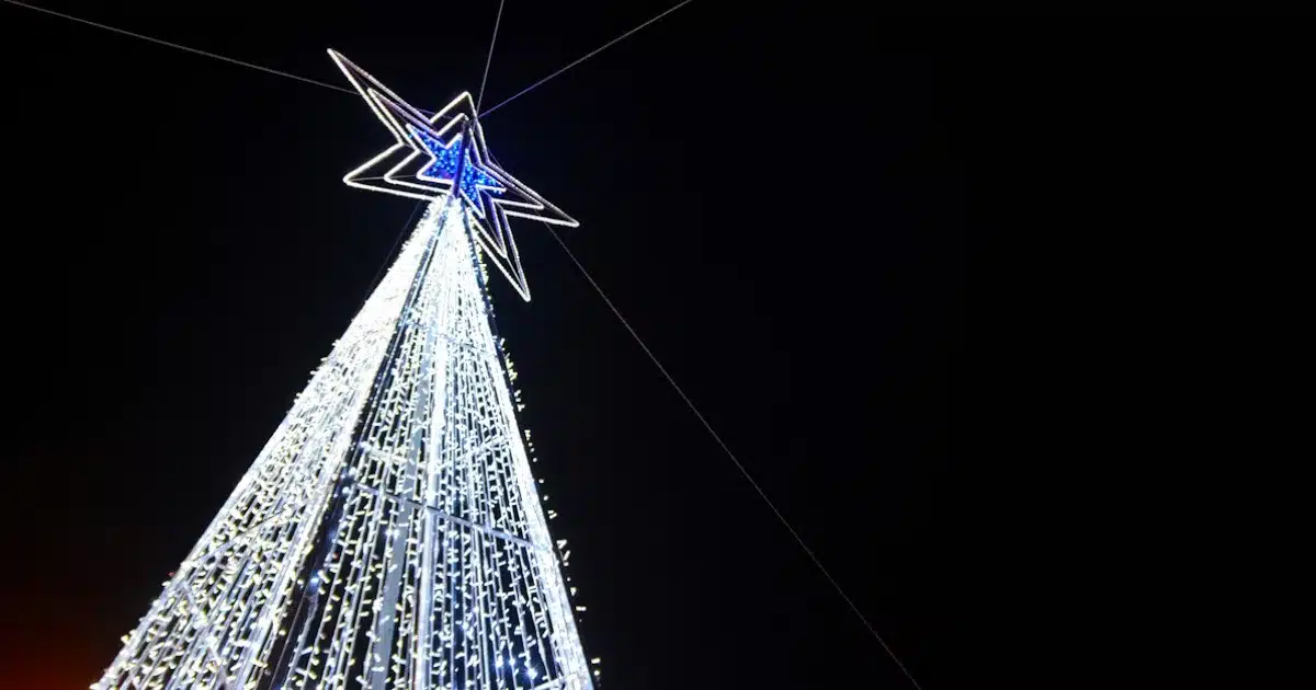 Árvore natalina iluminada noturna com estrela no topo.