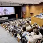 Conferência em auditório com palestrante e público atento.