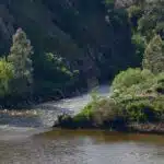 Rio cercado por vegetação verdejante e encostas rochosas.