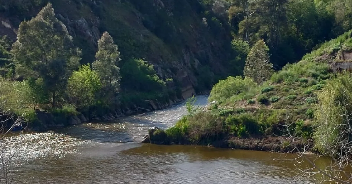 Rio cercado por vegetação verdejante e encostas rochosas.