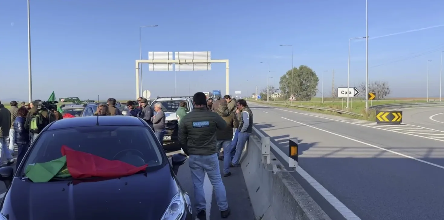 Manifestação bloqueando estrada com bandeira portuguesa.