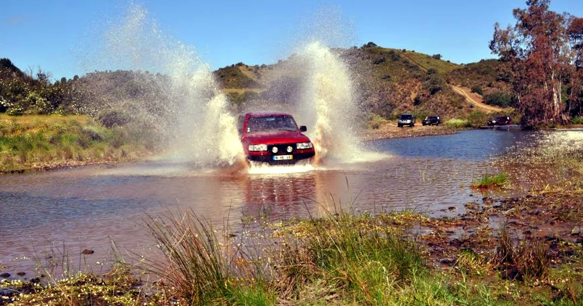 Carro atravessando rio rapidamente em terreno acidentado.