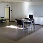 Sala de aula vazia com quadro branco e computador.