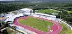 Estádio e pista de atletismo aéreos cercados por árvores.