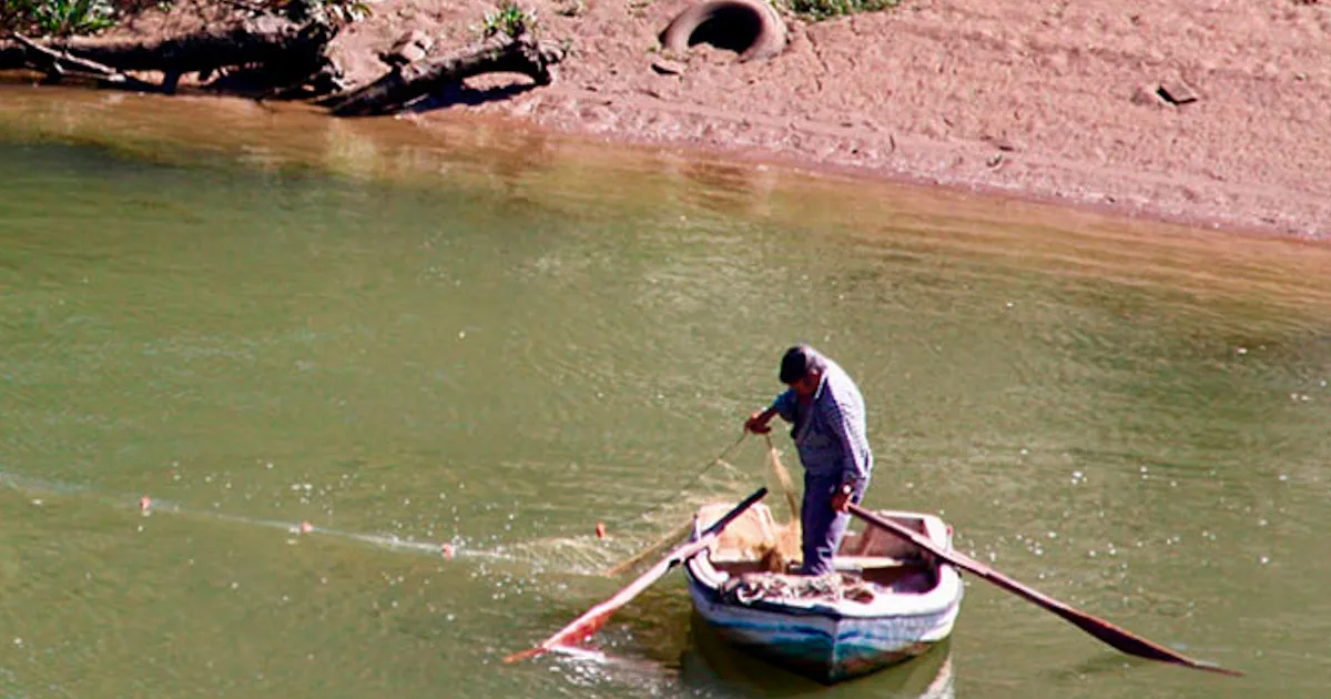 Pescador em barco no rio a lançar rede.