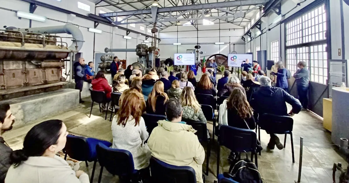 Conferência em espaço industrial com público sentado.