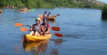 Pessoas praticando canoagem em rio ensolarado.