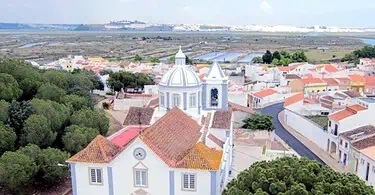 Vista aérea de vila portuguesa com igreja e rio.