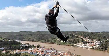 Homem praticando tirolesa sobre rio e cidade.